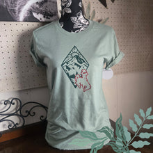 Light green t-shirt with a graphic design on a mannequin against a pegboard wall.