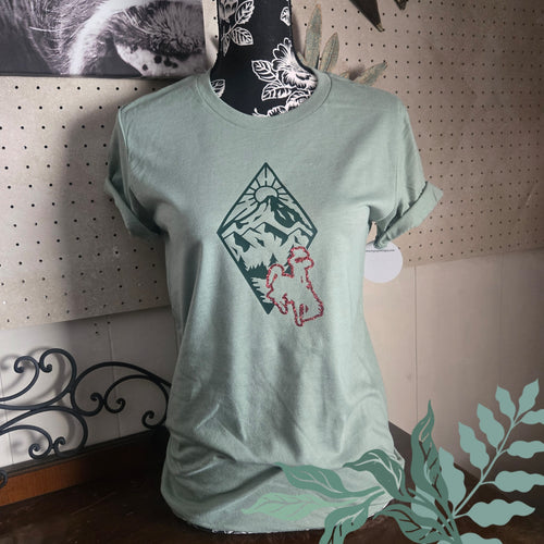Light green t-shirt with a graphic design on a mannequin against a pegboard wall.
